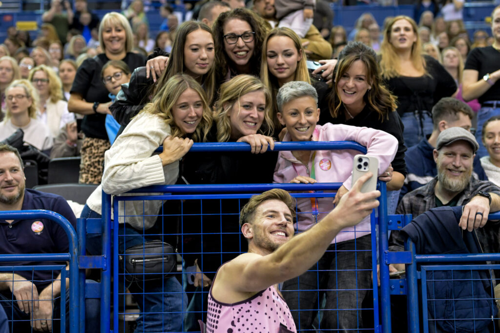 A fan leans over the barrier to take a selfie with a Netball Aid player