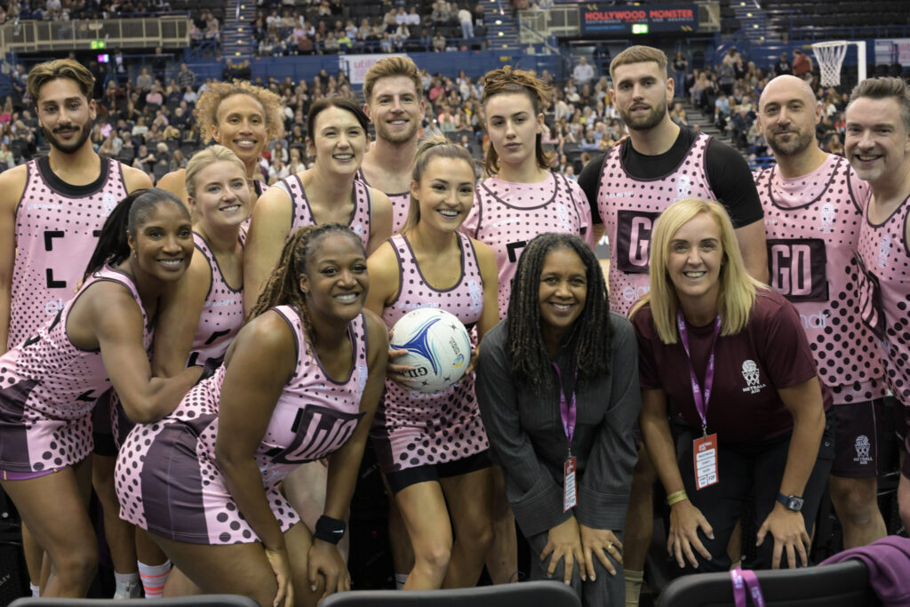 Players and guests in Netball Aid pink kit smile for a team photo